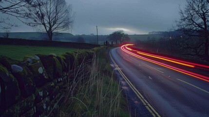 Poster - An old stone wall runs alongside the country lane while the vibrant light trails of passing cars bring life and energy to the scene.