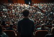 © SH Design - A man stands in front of a crowd of people in a large auditorium