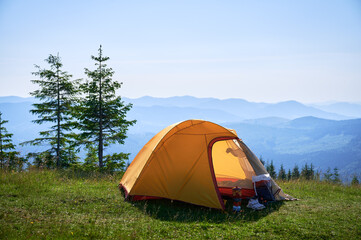 bright yellow tent with camping gear on grassy hillside, overlooking breathtaking panorama of blue-t
