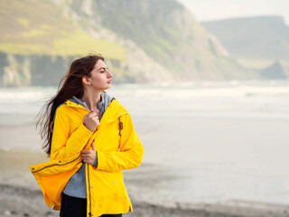 Wall Mural - Portrait of a young teenager girl in yellow jacket, nature background. Travel and tourism. The model has long hair and slim athletic body type. Trip to nature concept.