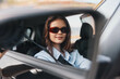 © SHOTPRIME STUDIO - Woman driving car, wearing sunglasses, looking out window at vehicle ahead, rearview mirror tilted up