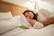 © Odua Images - A peaceful moment of a woman resting in bed, with her smartphone conveniently beside her