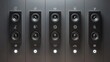 © Bushra - Five identical black audio speakers mounted vertically in a dark modern wall panel system with indicator lights.
