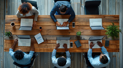 Poster - An overhead view of a collaborative office workspace, showing four diverse professionals seated around a wooden table. The individuals are deeply engaged in their tasks.