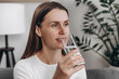 © Yura Yarema - Close up of healthy cute young female sitting on couch in living room drinking water for good health, such as helping to digest food. Makes heart work better, stimulates digestive system concept