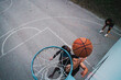 © Studio Marmellata - A vibrant capture of three basketball players engaging under the hoop on a marked outdoor court framed by bright trees and open sky.