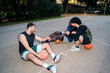 © Studio Marmellata - Teammates relax on the outdoor basketball court, sharing laughs and camaraderie during a break, with a focus on teamwork and friendship in a serene environment.