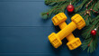 © Fotosova - The concept of Christmas and New Year fitness. On a dark blue wooden background there are two yellow dumbbells in knitted covers, Christmas tree branches with garlands and toys. Place for the text