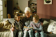 © AnnaStills - Elderly woman reading story to two granddaughters on couch in cozy living room illuminated by warm light reflecting familial bond and love