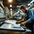 © Murda - Man inspecting printed papers on large machine.