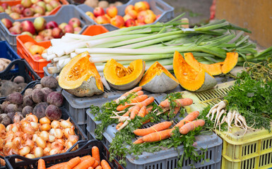 A vibrant market stand displaying fresh vegetables including carrots, onions, pumpkins, leeks, and parsley roots. A colorful variety showcasing healthy, organic produce.