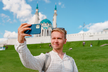 Wall Mural - A young male tourist takes a selfie with a smartphone against the background of a Kul Sharif mosque on a cloudy day, Kazan, Russia