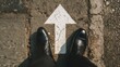 ©   - Step Forward: A person stands confidently with business shoes pointing directly at a large, bold white arrow painted on a rough brick surface, symbolizing a clear direction forward.