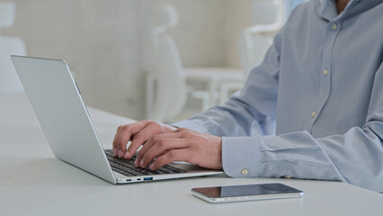 Moving shot Arabian Indian businessman ethnic smiling man working laptop male business employer programmer coding computer program software typing project remote job with mobile phone on office table