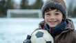 ©  Dreamy Shots - Smiling boy holding snowy soccer ball on winter day, dressed in warm jacket and knit hat, playful expression, outdoor fun, childhood joy, active lifestyle, cheerful mood