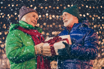 Wall Mural - Two people old parents grey white hair married couple meet 2021 year x-mas christmas give dream wish gift boxes under tinsels garland evening lights outdoors wear coat scarf