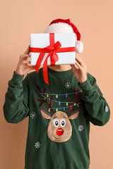 Wall Mural - Young man in Santa hat with Christmas gift on beige background