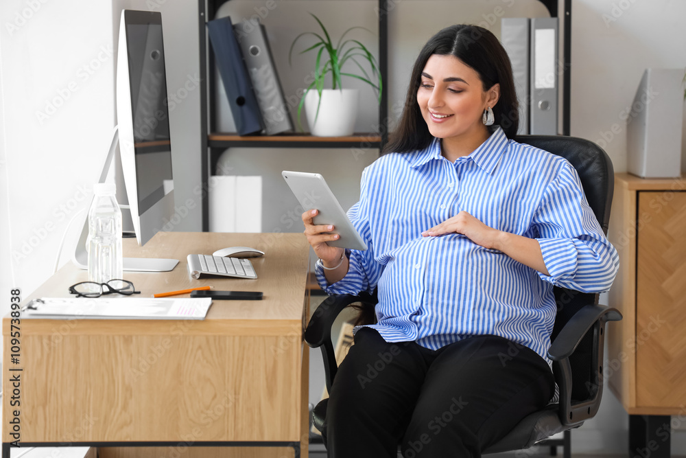 Pregnant businesswoman with tablet computer working at table in office
