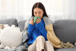 © Pixel-Shot - Beautiful young woman in blue knitted sweater with blanket and cup of tea sitting on sofa at home