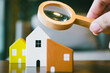 © sommart - Hand holding magnifying glass and looking at house model, house selection, real estate concept.
