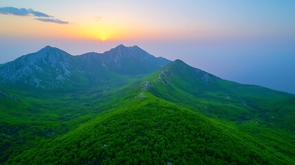 Wall Mural - Breathtaking View of Lush Green Mountains Under a Vibrant Sunset Sky with Gentle Mist Over the Horizon and Serene Natural Landscape