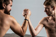 © Yevhen - Arm wrestling. Two man's hands clasped arm wrestling, strong and weak, unequal match. Heavily muscled bearded man arm wrestling a puny weak man
