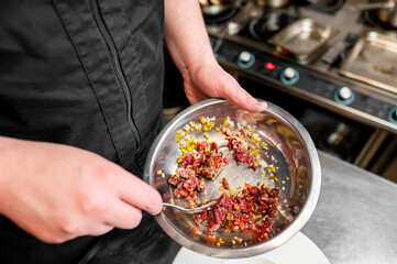 Wall Mural - Close-up of a chef’s hands holding a stainless steel bowl with mixed colorful ingredients in a professional kitchen setting. Ideal for culinary themes, food preparation