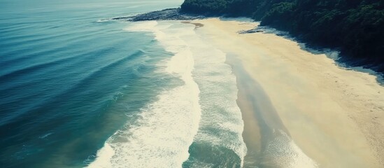 Poster - Aerial view of tranquil beach with gentle ocean waves lapping sandy shore and lush greenery in the background on a sunny day