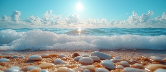 Aufkleber - Scattered pebbles on sandy beach with foamy waves and bright sunlight shining over calm blue sea under a clear sky