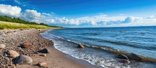 Aufkleber - Serene rocky beach landscape under a clear blue sky with gentle waves lapping at the shore and lush greenery in the background