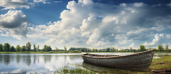 Poster - Serene rural river landscape featuring an old wooden boat under a dramatic sky with fluffy clouds and lush greenery in the background