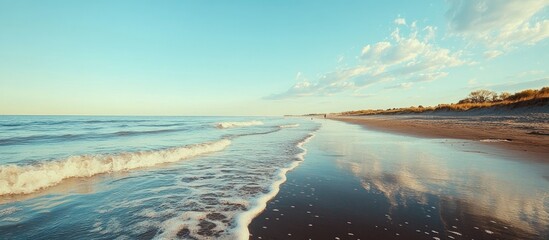 Poster - Tranquil beach landscape with clear water and soft waves reflecting a serene sky at sunset