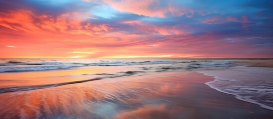 Aufkleber - Vibrant sunset colors reflected on calm ocean waters with sandy beach in serene coastal landscape.