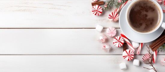 Poster - Cozy winter hot chocolate with marshmallows and peppermint candies in a white mug top view on wood background with space for festive text