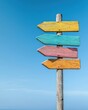 © Somporn - A colorful wooden signpost with multiple arrows pointing in different directions against a clear blue sky.