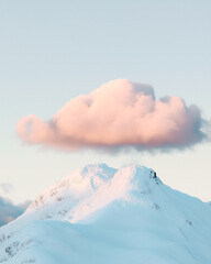 Wall Mural - Summit of a mountain covered in snow with a cloud right above at sunrise.