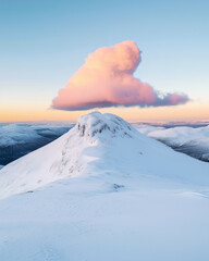 Wall Mural - Summit of a mountain covered in snow with a cloud right above at sunrise.