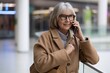 © Ivan Traimak - Senior woman wearing glasses engages in a phone conversation at a modern shopping center during the day
