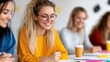 © Pinklife - A cheerful young woman, wearing a yellow sweater and glasses, sits in a bright indoor setting, enthusiastically engaged in a writing task alongside others.