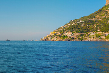 Wall Mural - The photo captures a sunny view of Amalfi, showcasing the town's colorful buildings, steep cliffs, and vibrant coastline under a clear blue sky on a bright day.