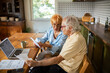 © Marko Geber - Concerned senior couple reading bills on kitchen table with laptop