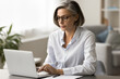 © fizkes - Focused pretty mature business woman in elegant glasses typing on laptop, working at computer in home office, using Internet technology for freelance job communication