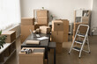 © fizkes - Warehouse office workplace with laptop computer on work desk among heaps of cardboard boxes and stepladder. Internet shop storage room interior with stacked paper packages, no people