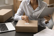 © fizkes - Mature entrepreneur woman checking bar code on cardboard box, using tablet, working in ecommerce storage, processing Internet shop order, packaging parcel for customer. Cropped shot