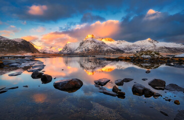 Wall Mural - landscape with snowy mountains reflecting on calm water with stones and colorful sky with clouds at 