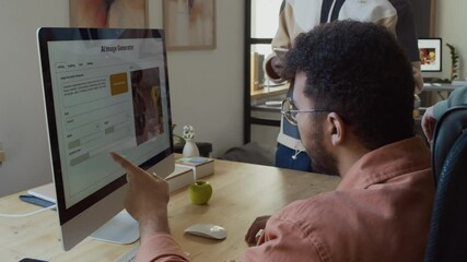 Medium closeup of young biracial male developer sitting at desk during meeting with colleagues on project, studying interface of AI image generation software on computer screen