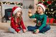 © New Africa - Little kids in Santa hats with Christmas ball on floor at home