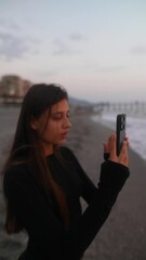 Wall Mural - A Young Woman Enjoying the Beauty of Capturing Sunset Moments by the Beach Shoreline