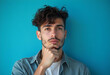© PTD - thoughtful young man with curly hair poses against blue background, showcasing contemplative expression. His casual style adds to relaxed vibe of image