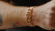 © PaulShlykov - Golden chain bracelet worn on arm showcasing intricate links and tattooed skin during casual indoor setting